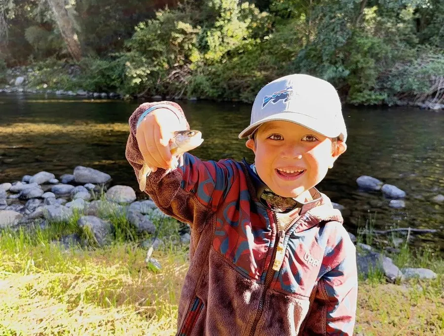 Niño sonriendo mientras muestra su primera trucha capturada